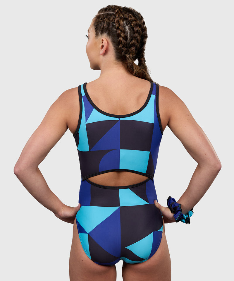 Plum Gymnast wearing the Plum Eclipse Leotard in bold blue geometric print with a stylish keyhole back cutout.  Eclipse Keyhole Leotard