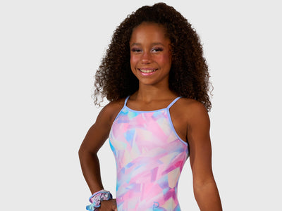 The Plum Ice Prism Leotard features pastel shades of pink, white, grey, and purple with spaghetti straps for freedom of movement. Made from breathable fabrics and smooth seams. Includes a matching scrunchie. 