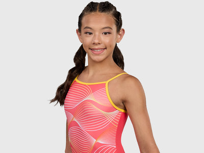 Gymnast rocking the Plum Solar Spaghetti Strap Leotard in bright coral with a wave pattern and matching scrunchie. 