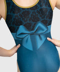 Close-up of a child wearing a blue and black gymnastics leotard with a large satin bow print at the waist, black floral lace on the upper chest, and gold trim at the neckline.