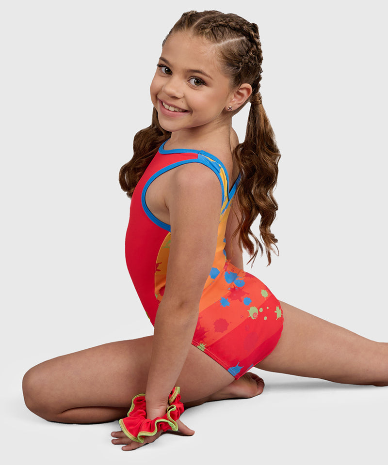 Gymnast wearing the Plum Splat Spaghetti Strap Leotard with a bold red front and a colorful ombré paint-splatter back. 