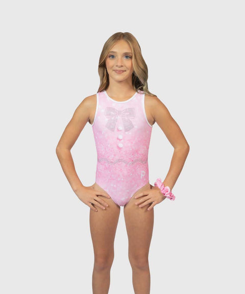 A young girl modeling a pink sleeveless leotard with a bow and lace print, standing against a light gray background.