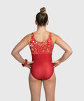 A woman viewed from behind wearing a red one-piece gymnastics leotard with gold floral and star patterns across the upper back and shoulders, set against a solid light gray background.