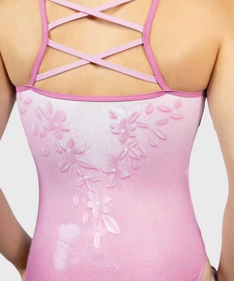 Close-up back view of a pink leotard with floral applique and crisscross lace-up straps, shown on a model against a light gray background.