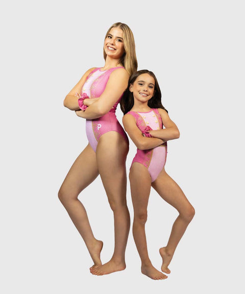 Two models, an adult woman and a young girl, standing back-to-back in matching pink and white leotards against a light gray studio background.
